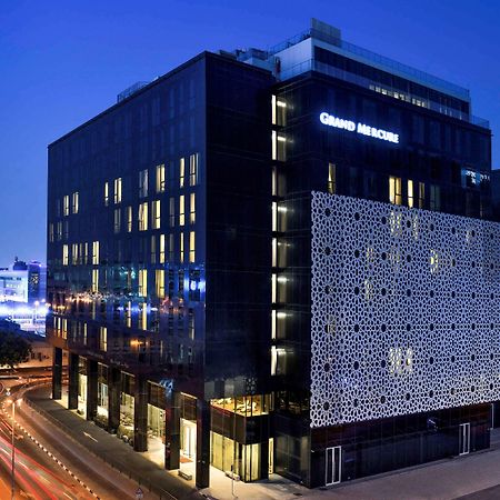 Grand Mercure Dubai City Exterior photo The photo shows a modern building at night, featuring a sleek, contemporary design. The building has a large facade with a distinctive patterned wall on one side. Illuminated signs display the name "Grand Maison." Surrounding the building, there are 
